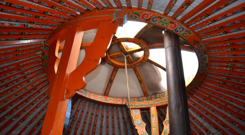 Interior ceiling of a Mongolian ger with a toono crown window at the center, two support pillars, and radiating roof poles.