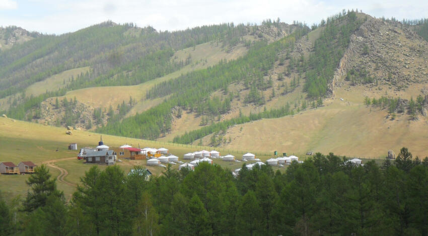 A tourist ger camp in Terelj National Park, with rows of traditional white Mongolian gers arranged on a green valley floor.