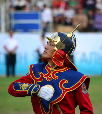 Honor guard in ceremonial red and blue uniform, plumed helmet with gold decorations
                            at Mongolian Naadam festival.
