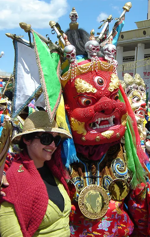 Woman posing with a masked Tsam dancer in traditional costume at a Buddhist festival in Ulaanbaatar