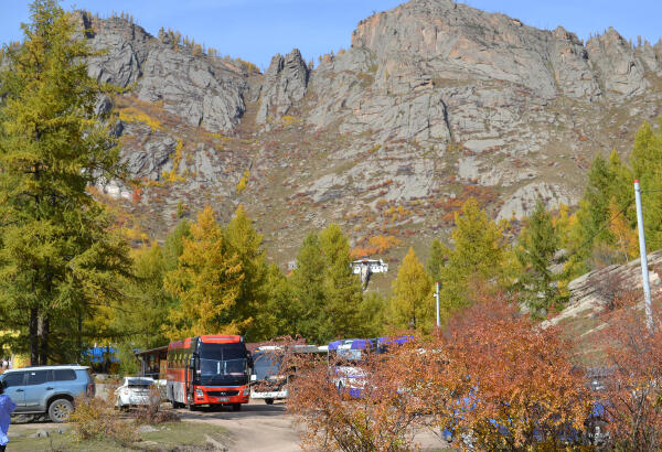 Tourist buses and autumn trees at the foot of the Ariyabal Buddhist meditation temple, perched on a mountainside.